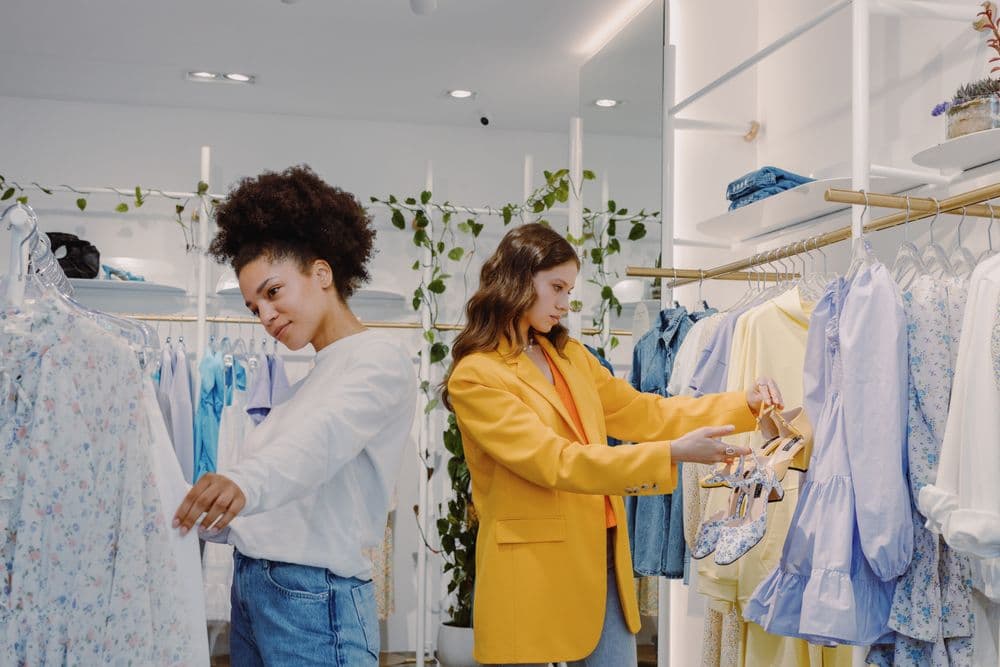 Two customers looking through clothes on a rail with help from a shop assistant